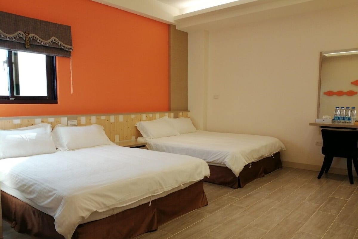 Quarto de hotel com duas camas de solteiro, uma secretária pequena e uma janela com cortina.