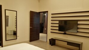 Un dormitorio moderno con una cama grande, un televisor en la pared, un banco y una puerta que da a otra habitación.