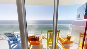 Un balcón con vista al océano, con sillas y una mesa azul y amarilla.