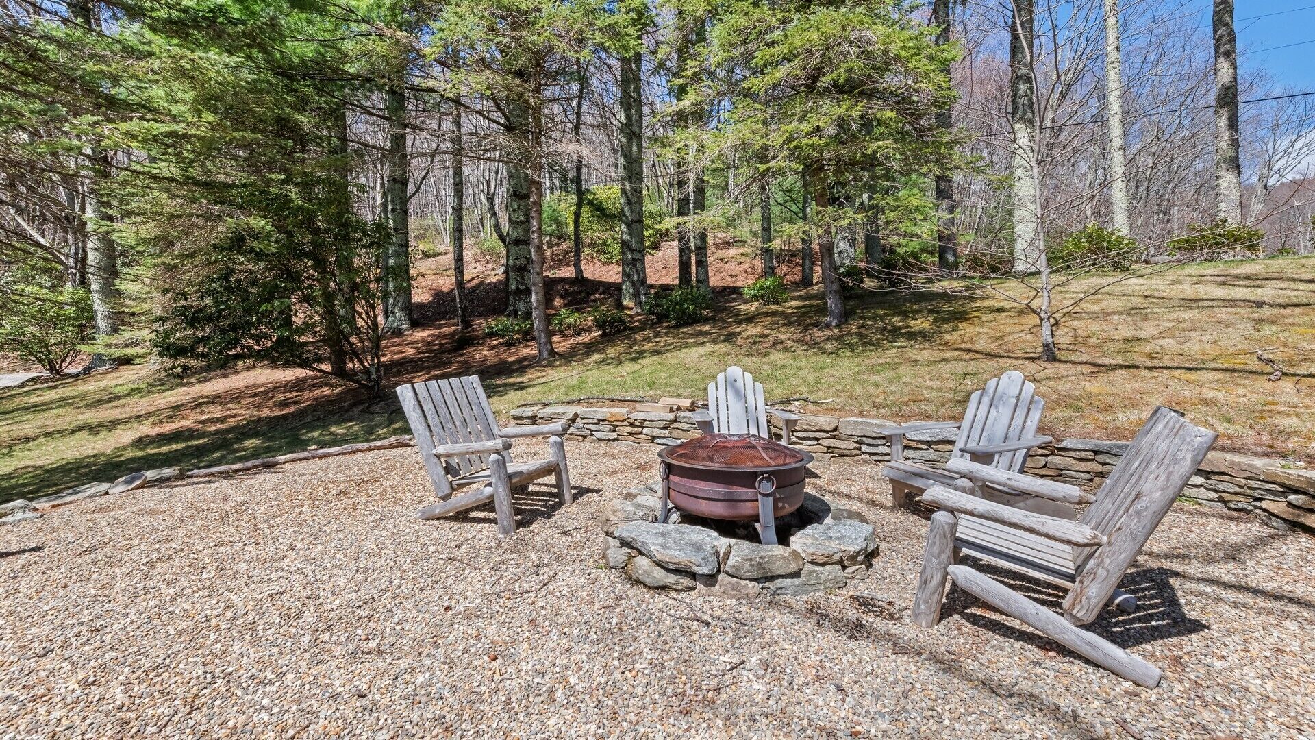 Un espace circulaire aménagé avec des fauteuils Adirondack disposés autour d’un foyer en pierre.