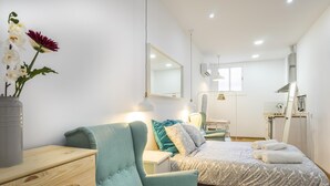 Une chambre à coucher moderne avec un lit, une chaise, une commode, un miroir et un vase rempli de fleurs.