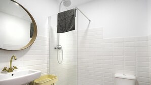 Une salle de bain avec un lavabo blanc, un meuble-lavabo de couleur dorée, une douche avec une porte en verre et des toilettes blanches.