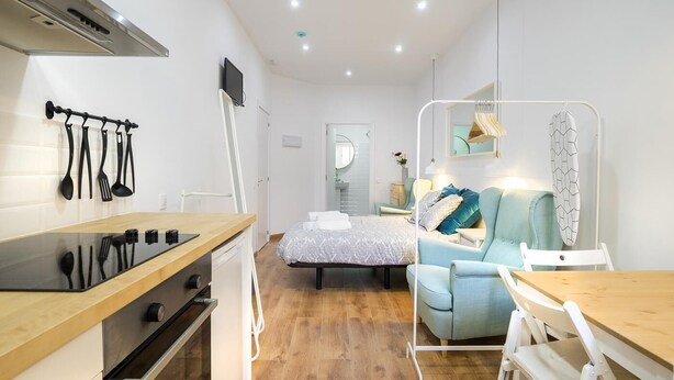 Une chambre d’hôtel compacte comprenant un coin cuisine, un lit avec une couette à motifs, un petit coin salon et un miroir au-dessus du lit.