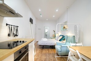A compact hotel room with a kitchenette, a bed with a patterned duvet, a small seating area, and a mirror above the bed. - Hotelito Boutique Mercat 1 (Hospitalet de Llobregat, Barcelona)