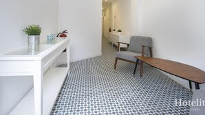 A hotel room with a white desk, a chair, a small table, a potted plant, a fire extinguisher, and a patterned floor. - Hotelito Boutique Camp Nou 2 (Hospitalet de Llobregat, Barcelona)