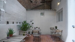 A small patio area with a wooden table and chairs, surrounded by potted plants and a small window. - Hotelito Boutique Camp Nou 2 (Hospitalet de Llobregat, Barcelona)