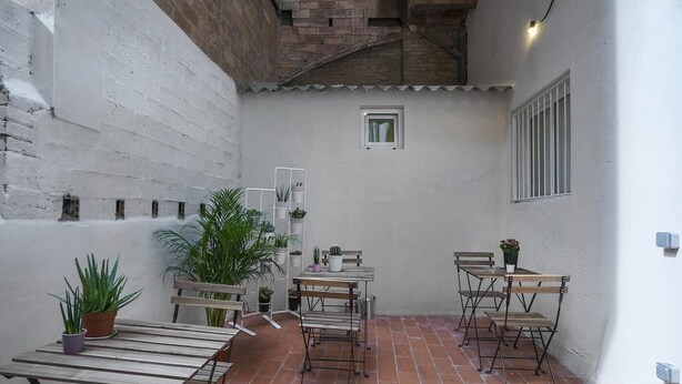 A small patio area with a wooden table and chairs, surrounded by potted plants and a small window. - Hotelito Boutique Camp Nou (Hospitalet de Llobregat, Barcelona.)