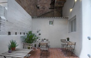 A small patio area with a wooden table and chairs, surrounded by potted plants and a small window. - Hotelito Boutique Camp Nou (Hospitalet de Llobregat, Barcelona.)