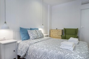 Un dormitorio con cama, mesitas de noche, cómoda, silla y lámpara.