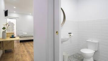 A modern bedroom with a bed, bedside table, and a small desk with a vase and flowers.