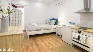 Une chambre d’hôtel de taille réduite, comprenant un lit, une table de chevet, une lampe et une kitchenette.