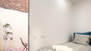 Une chambre avec un lit, une chaise, une échelle ornée de plantes et une vue sur un mur de briques.