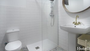 A bathroom with a toilet, a shower with a glass door, a sink with a gold faucet, and a mirror with a wooden frame. - Hotelito Boutique Mercat 6 (Hospitalet de Llobregat, Barcelona.)