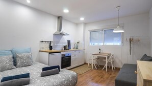 Ein kompakter Wohnbereich mit Küchenzeile, Essplatz und einem Bett mit gemusterten Bettwaren.