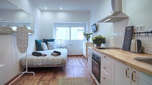 Une chambre d’hôtel de taille réduite, comprenant un lit, une petite kitchenette, une fenêtre et un ventilateur de plafond.