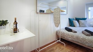 Une chambre à coucher moderne avec un lit, une table de chevet sur laquelle se trouvent une bouteille et des verres, un miroir et un portant à vêtements suspendu.