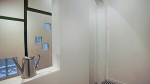 Une pièce avec une fenêtre, un pichet en métal et un mur orné de motifs géométriques.