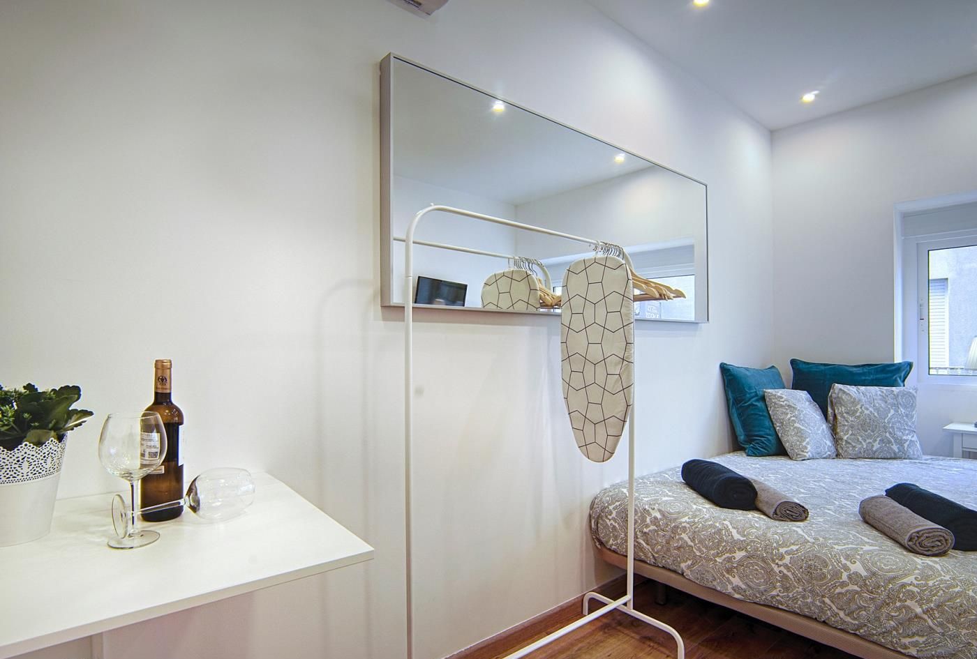 Un dormitorio moderno con una cama, una mesita de noche con una botella y vasos, un espejo y un perchero.