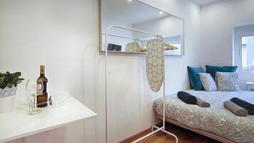 Un dormitorio moderno con una cama, una mesita de noche con una botella y vasos, un espejo y un perchero.
