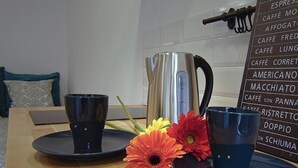 Uma bancada de cozinha com uma cafeteira, duas xícaras e um arranjo de flores.