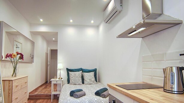 Quarto de hotel pequeno com cama, mesa de cabeceira, luminária, cozinha compacta e ar condicionado.