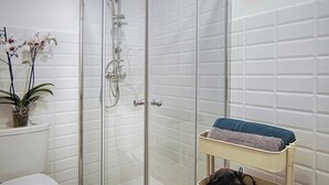 Chuveiro envidraçado com chuveiro manual e torneira fixa na parede.