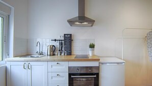 A modern kitchen with white cabinetry, a stainless steel range hood, a built-in oven, and a coffee machine.
