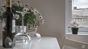 A bottle of wine, a wine glass, and a vase with flowers on a table by a window.