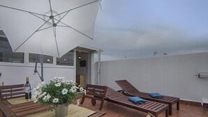 Eine Terrassengruppe mit Tisch, Stühlen, einem großen Sonnenschirm und einer Blumenkomposition.