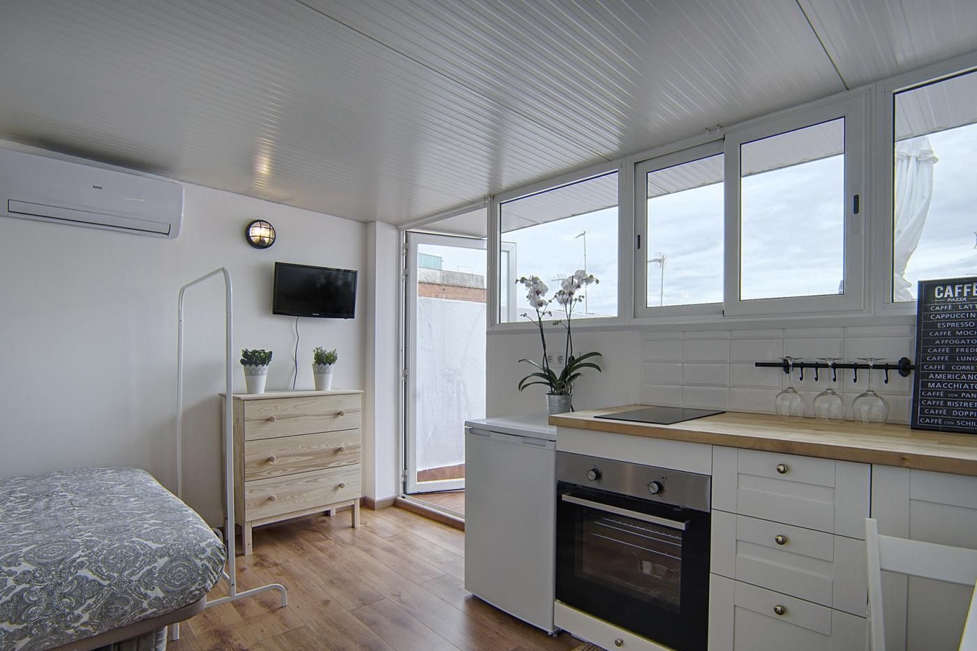 Una kitchenette compacta con horno integrado, un lavamanos pequeño y ventana con vistas a un balcón.