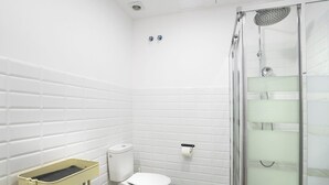 Une salle de bain avec des carreaux de céramique blancs rectangulaires, des toilettes, une douche avec une porte en verre et une étagère jaune.