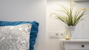Une chambre à coucher avec un lit, une table de chevet ornée d’une plante et un mur blanc équipé de prises électriques.