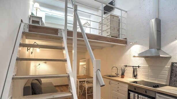 Ein kompaktes Hotelzimmer mit Küchenzeile, einer kleinen Essecke und einer Treppe, die zu einer Mansardenwohnung führt.