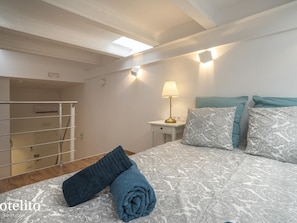 A bedroom with a bed, a nightstand with a lamp, a wardrobe, and a window with natural light.