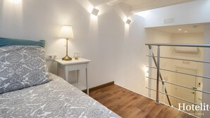 A hotel room with a bed, a bedside table with a lamp, a small nightstand, and a staircase leading to an upper floor. - Hotelito Boutique Cinca 3 (Hospitalet de Llobregat, Barcelona)