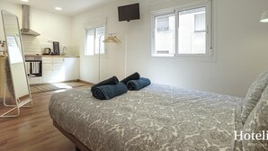 A bedroom with a bed, a TV mounted on the wall, and a kitchen area visible through an open door. - Hotelito Boutique Cinca 4 (Hospitalet de Llobregat, Barcelona)
