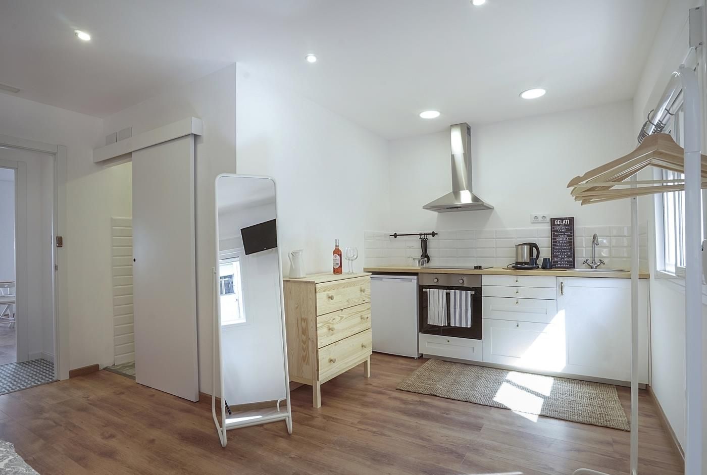 A modern kitchen with white cabinets, a stainless steel range hood, and a wooden countertop.
