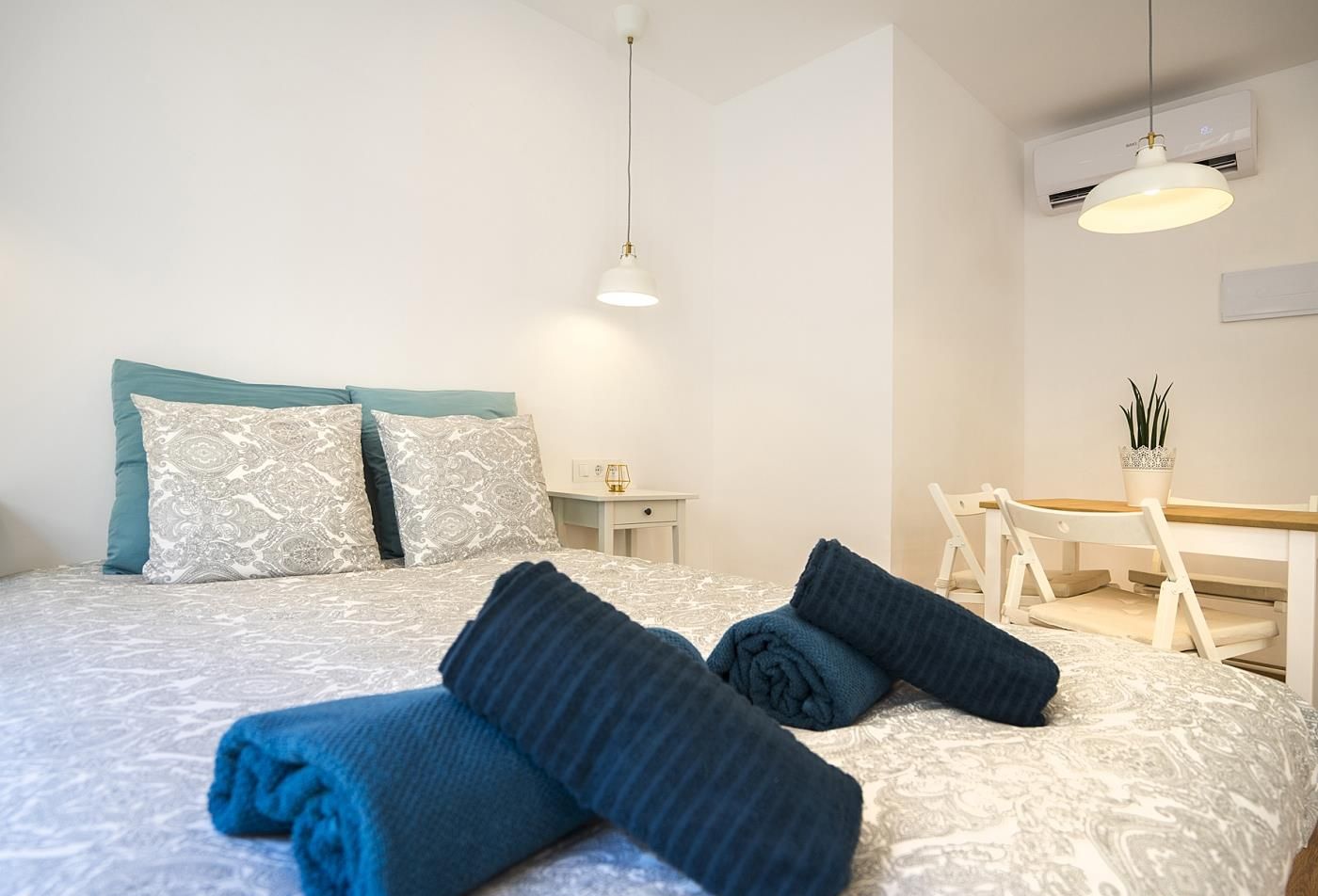 A hotel room with a neatly made bed, a desk with a chair, and a hanging light fixture.