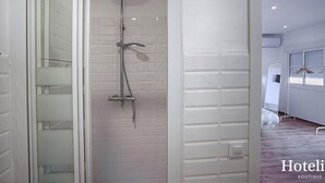 Un baño moderno con cabina de ducha de vidrio, paredes con azulejos blancos y un cabezal de ducha visible.