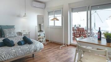 Una habitación de hotel moderna con una cama, un escritorio pequeño, una mesa de comedor con sillas, una planta en maceta y vistas al exterior.