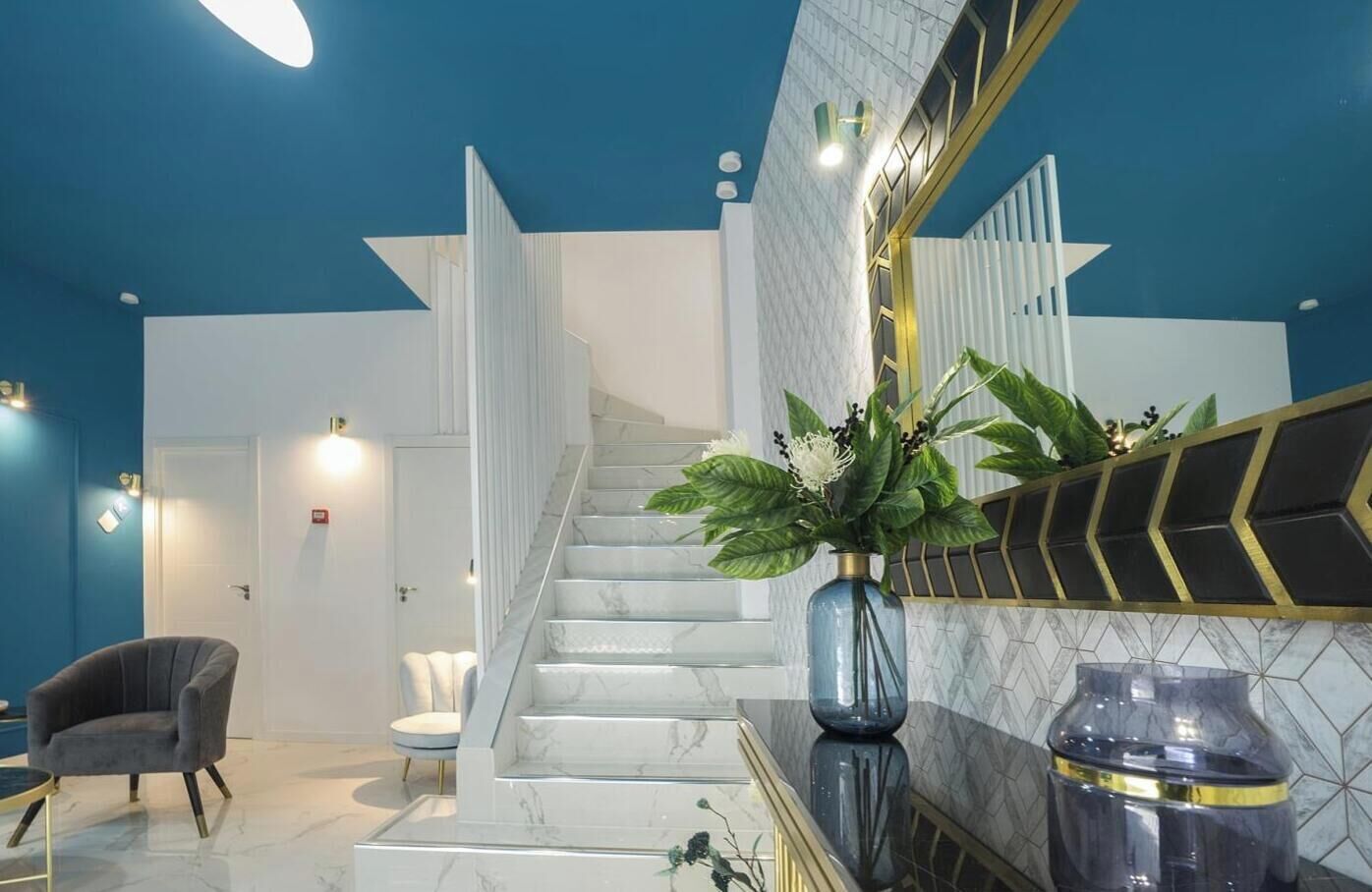 Un lobby moderno de hotel con una escalera de mármol, una zona de estar y un espejo grande con detalles decorativos.