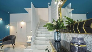 A modern hotel lobby with a marble staircase, a seating area, and a large mirror with decorative elements.