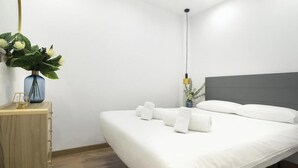 Quarto de hotel com uma cama, uma mesa de cabeceira com um vaso de flores e um abajur.