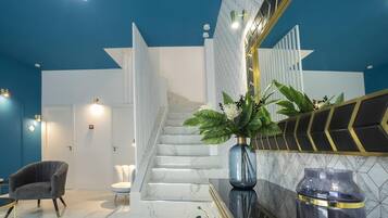 Un lobby moderno de hotel con una escalera de mármol, una zona de estar y un espejo grande con detalles decorativos.