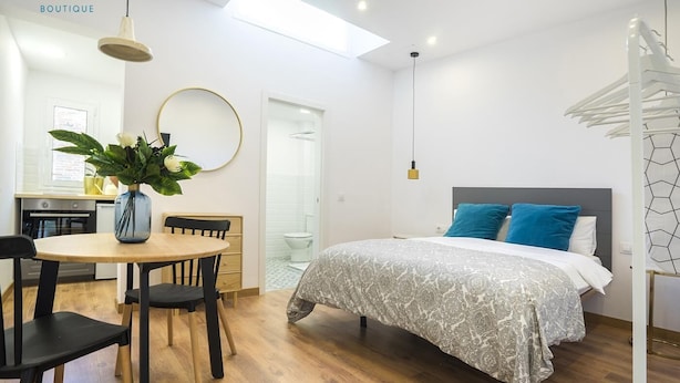 A modern hotel room with a bed, a dining table with chairs, a round mirror, and a potted plant. - Hotelito Boutique Badalona Mar 3 (Badalona)