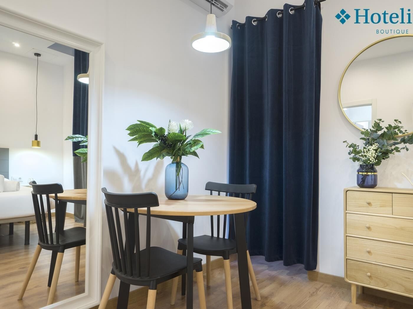 Habitación de hotel con comedor, espejo, cómoda y planta en maceta.