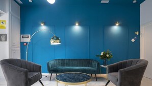 A room with a blue accent wall, a dark green sofa, two grey armchairs, a round marble coffee table, and a floor lamp. - Hotelito Boutique Badalona Mar 3 (Badalona)