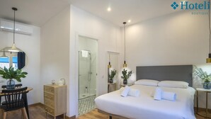 A modern hotel room with a large bed, a desk with a chair, a small table, a mirror, and a shower area. - Hotelito Boutique Badalona Mar 4 (Badalona, Barcelona)
