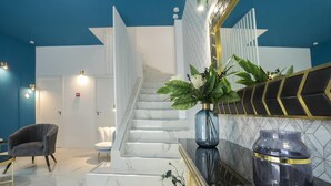 Un hall d’hôtel moderne avec un escalier en marbre, un espace salon et un grand miroir agrémenté d’éléments décoratifs.