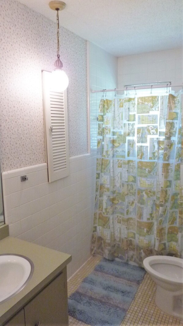 Un bagno con parete piastrellata in bianco, lavandino bianco, wc e tenda da doccia con motivo mappa.